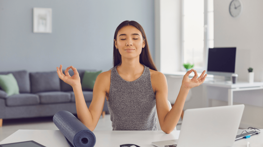 a woman meditating on a yoga mat in front of a laptop